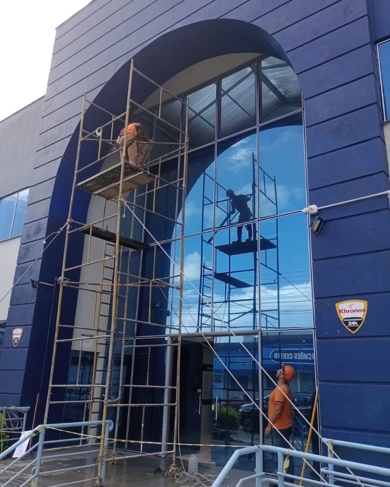Equipe técnica da Emkorp executando manutenção predial corporativa em fachada de vidro com uso de andaimes e isolamento de segurança em Joinville.
