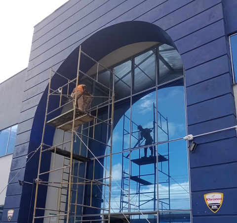 Profissional da Emkorp sobre andaime realizando manutenção predial na fachada azul com pele de vidro de um edifício comercial em Joinville.