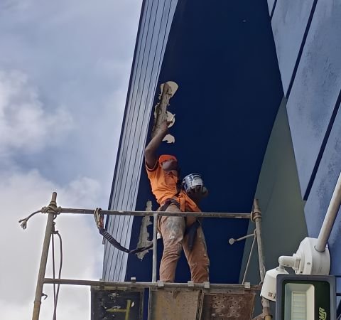 Profissional da Emkorp realizando pintura e recuperação de fachada sobre andaime metálico, utilizando equipamento de segurança para trabalho em altura, durante manutenção predial em Joinville.