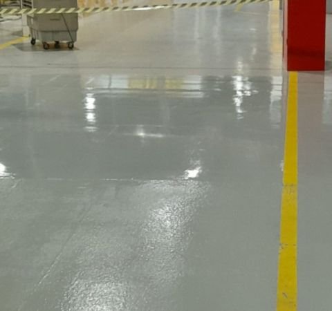 Detalhe de piso industrial com revestimento epóxi cinza de alto brilho e faixa de demarcação amarela de segurança, recém-aplicado pela Emkorp em Joinville.