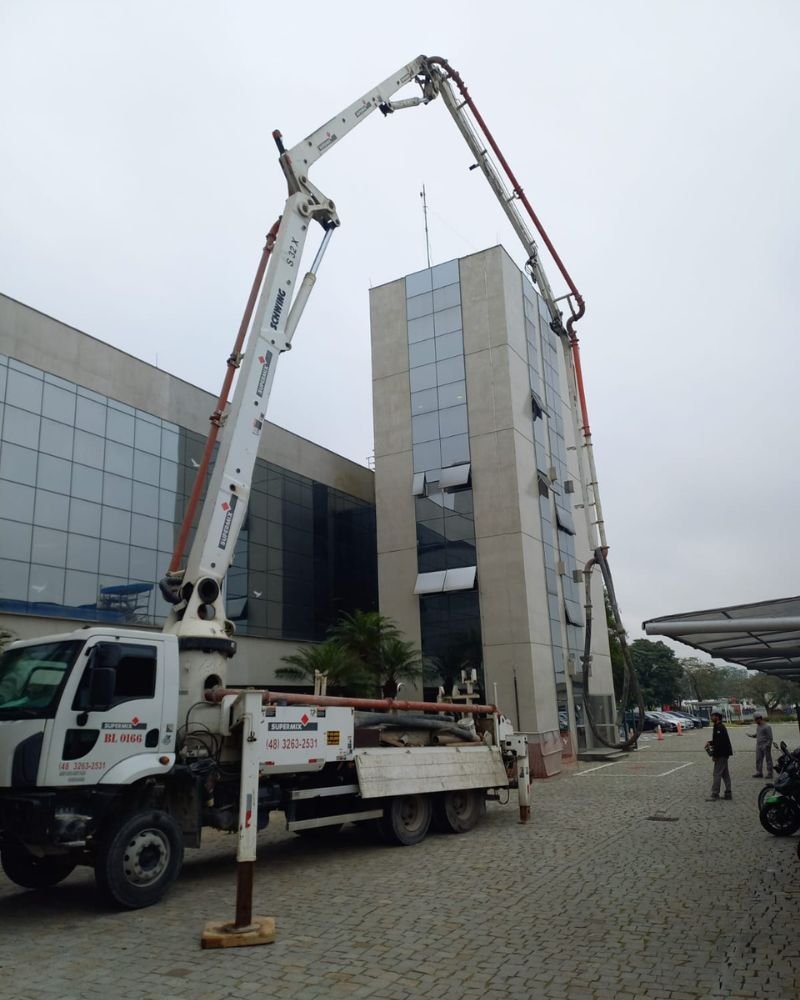 Caminhão bomba de concreto realizando operação de infraestrutura pesada em reforma corporativa de um edifício comercial de múltiplos andares, obra coordenada pela Emkorp em Joinville.