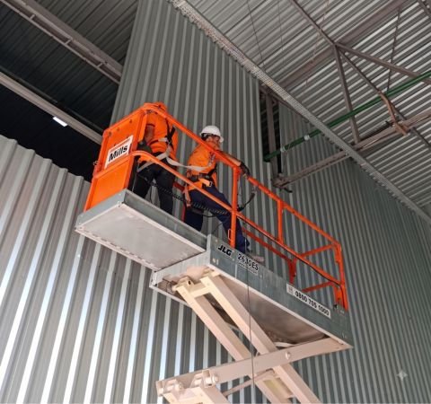 Sandro Kindermann, diretor da Emkorp, vestindo capacete branco e jaqueta laranja, analisando uma planta de engenharia durante o retrofit estrutural de um moderno escritório corporativo envidraçado.