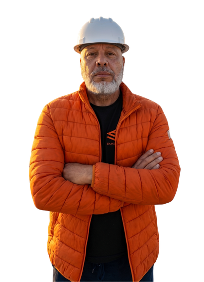 Retrato de Sandro Kindermann, diretor técnico da Emkorp, com os braços cruzados em postura de liderança, vestindo capacete branco de segurança e jaqueta laranja corporativa sobre fundo escuro.